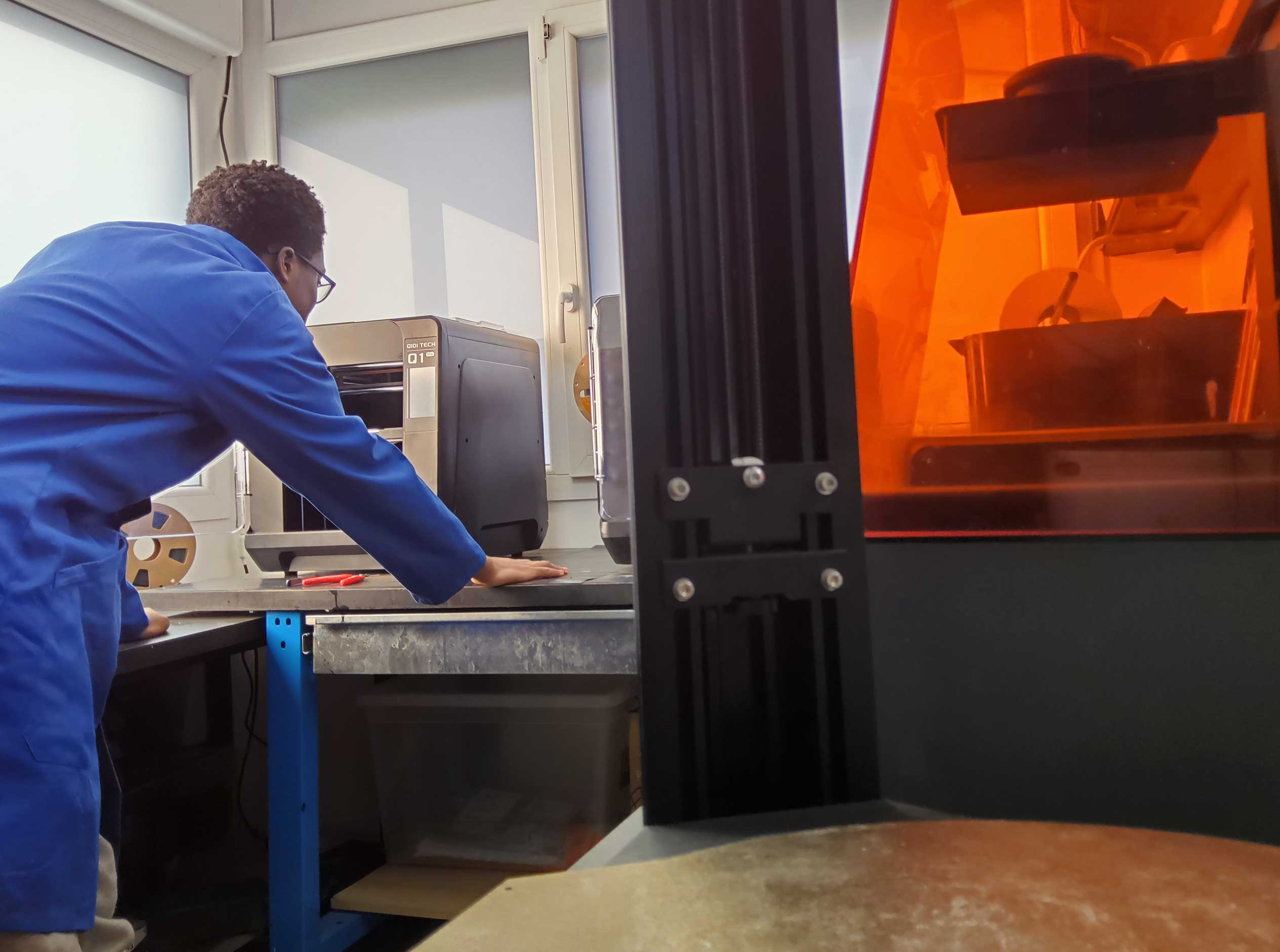 Header Article FAP & Design, une personne en bleu de travail analysant le fonctionnement d'une imprimante 3D
